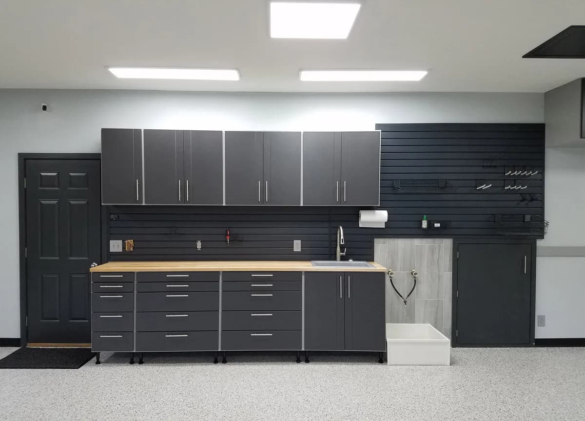 A finished two-car garage with grey storage cabinets, slatwall, and a coated floor.